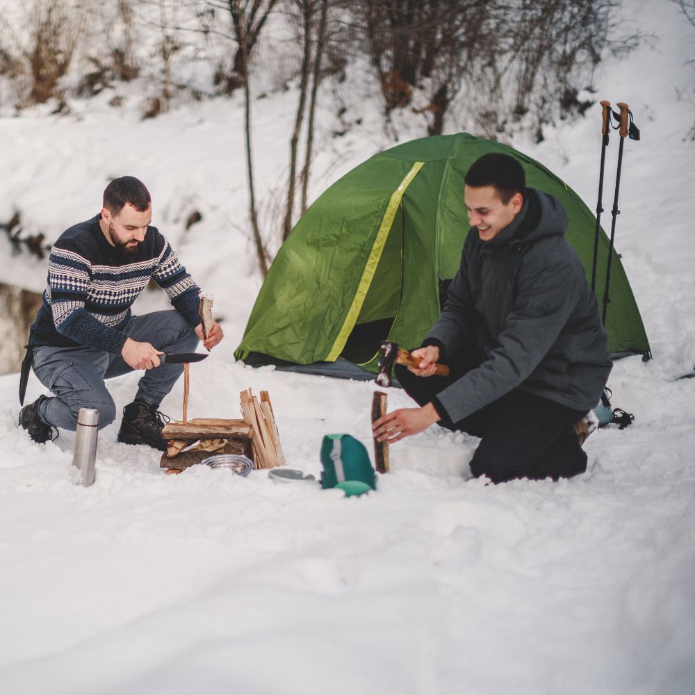 Two people camping in the snow with a green tent.