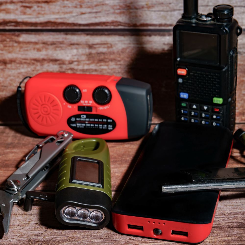 Collection of emergency supplies including a radio, flashlight, and power bank on a wooden surface.