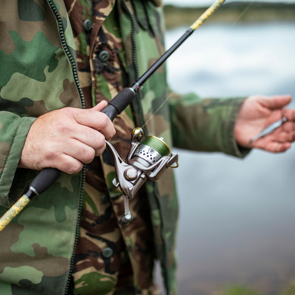 Person in camouflage jacket holding a fishing rod with a blurred natural background