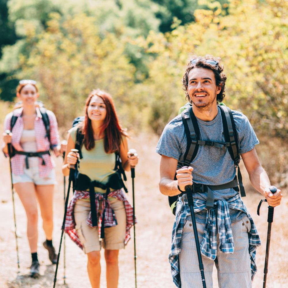 Three people hiking on a trail with backpacks and walking sticks.