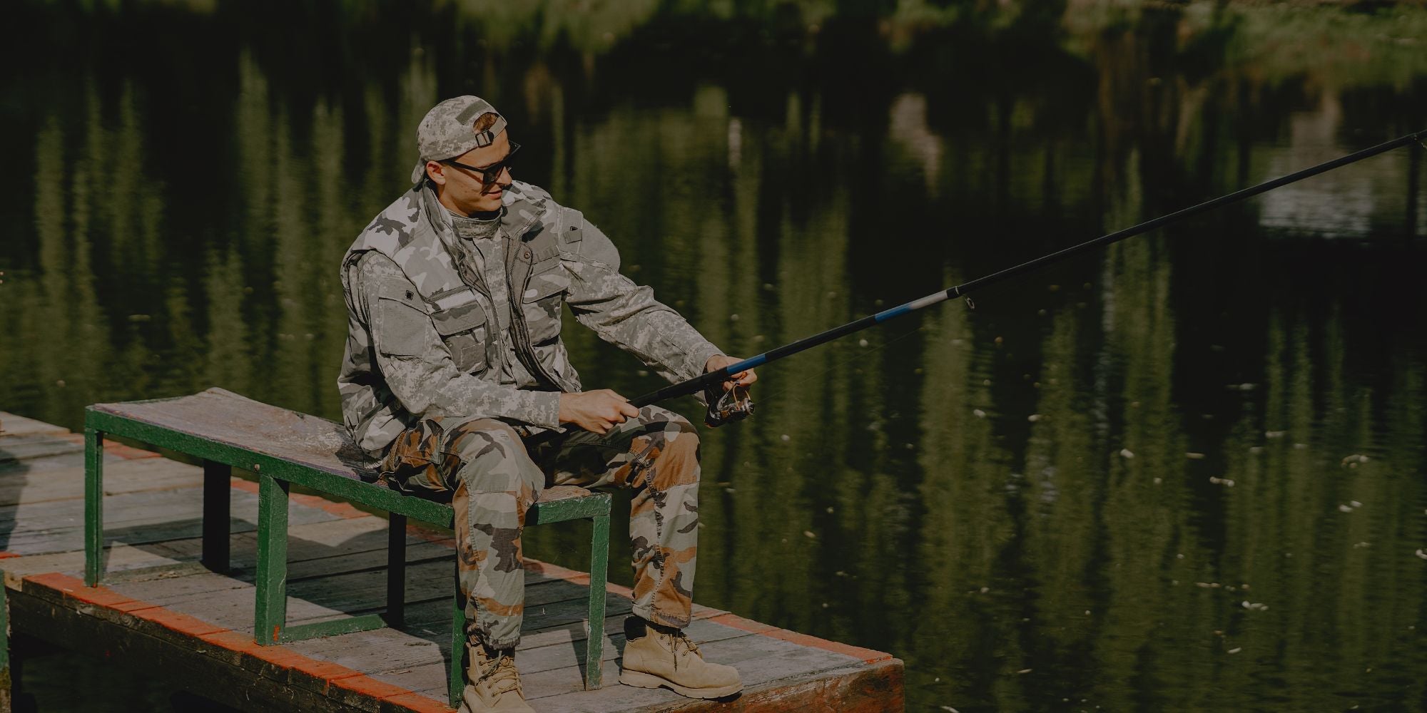 Man in camouflage fishing from a dock by a lake